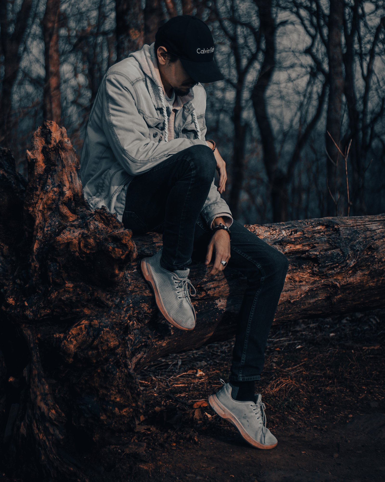 A man seated on a fallen tree in a forest, contemplative, black and white toned photograph